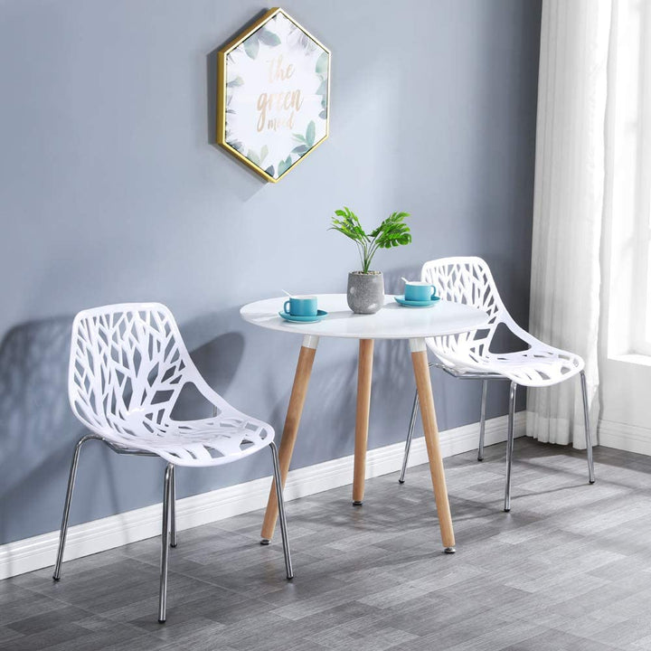 Set of two modern white plastic dining chairs with a bird nest design, featuring a metal frame, placed in a cozy dining setting with a white table and decorative plants in the background.